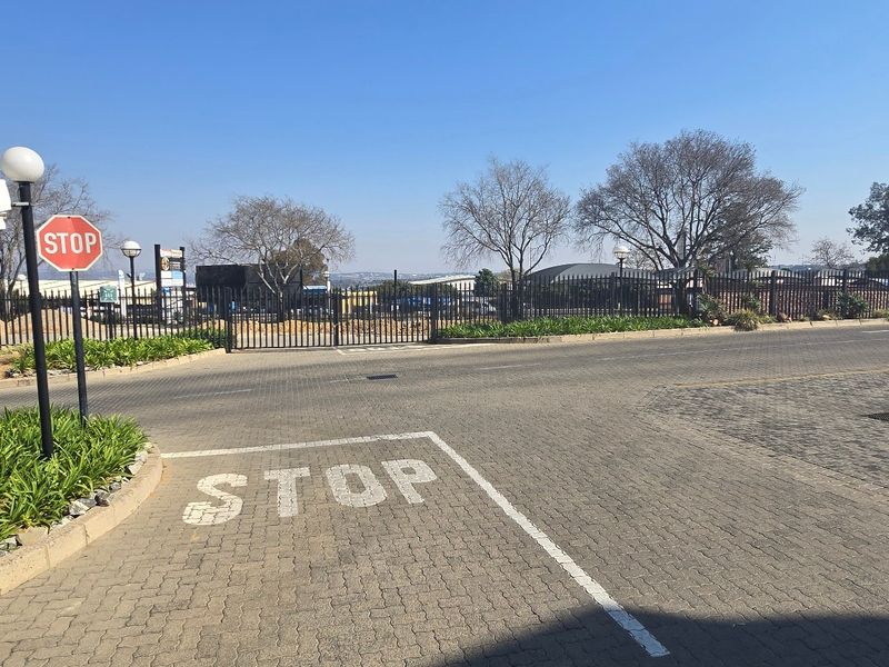 A paved industrial property entrance featuring secure metal fencing, gated access, and clear traffic signage.