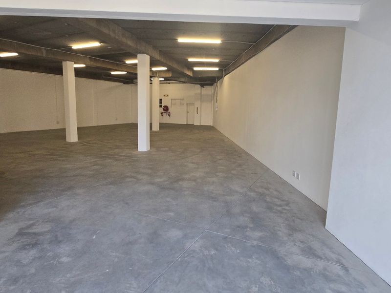 Spacious open-plan industrial warehouse area featuring polished concrete flooring, exposed concrete ceilings, and structural support columns, suitable for various commercial or storage uses.