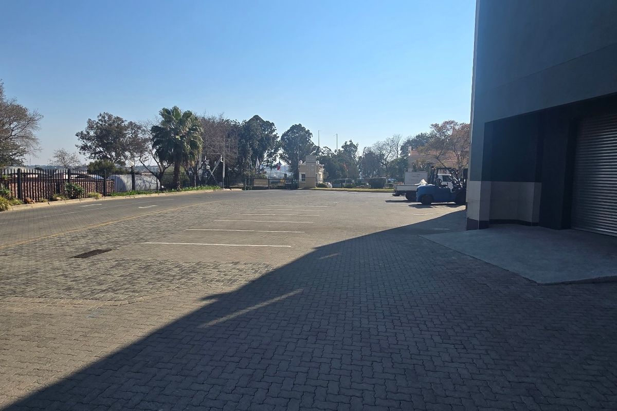 Industrial property exterior featuring a paved parking area, security fencing, and a large roller shutter door for loading access.