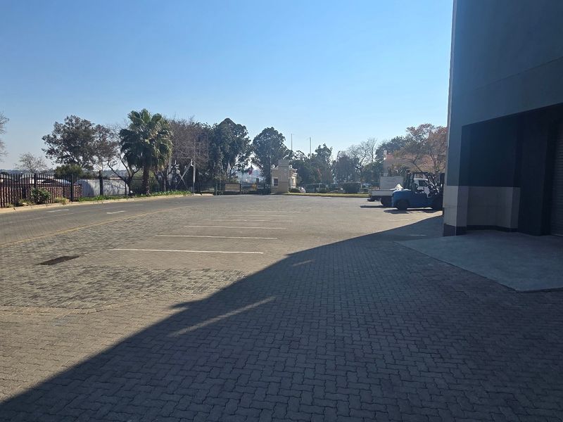 Industrial property exterior featuring a paved parking area, security fencing, and a large roller shutter door for loading access.