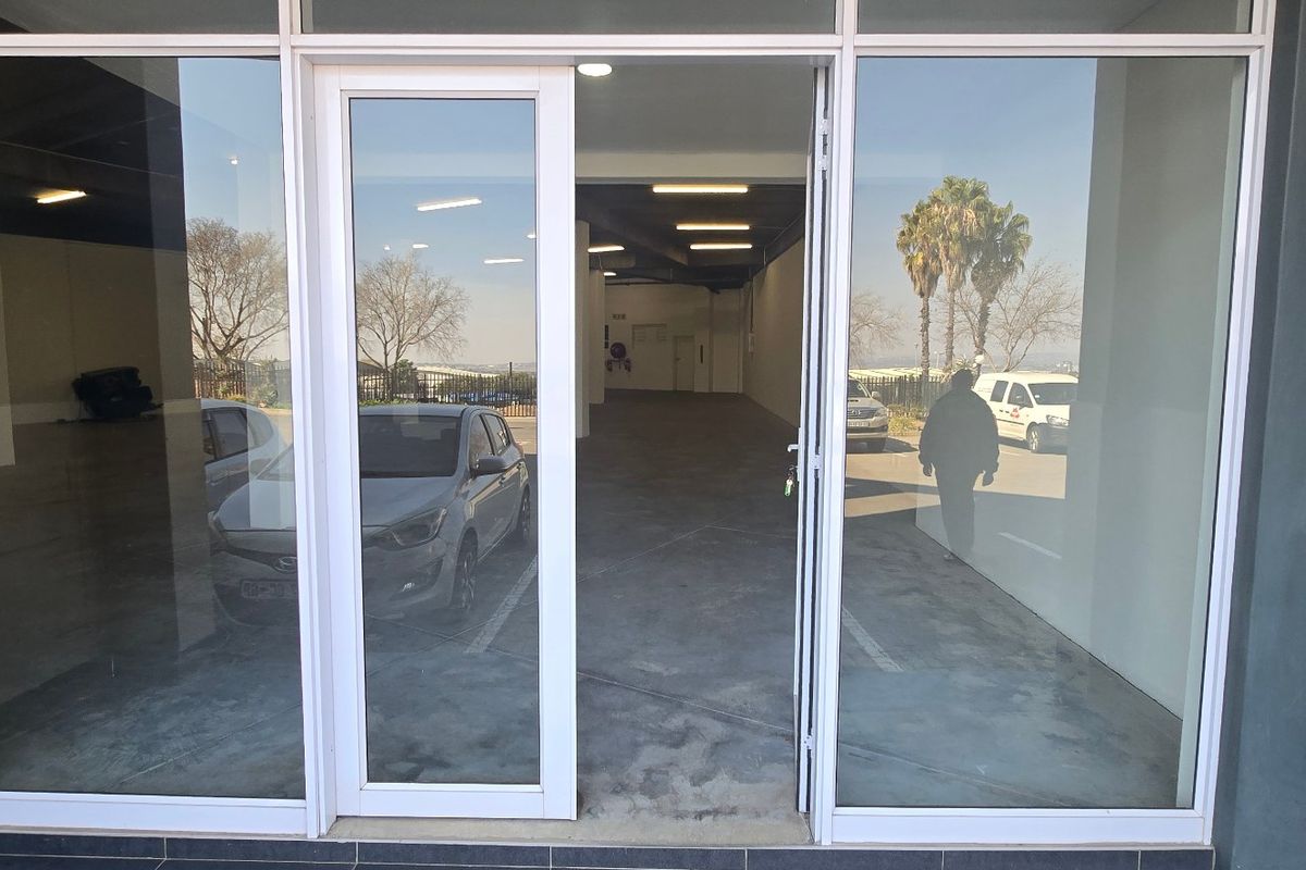 Modern industrial entrance featuring large glass storefront doors and windows, providing clear visibility into the spacious, open-plan interior with concrete flooring.