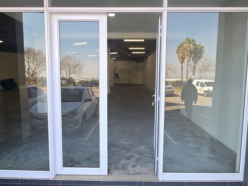 Modern industrial entrance featuring large glass storefront doors and windows, providing clear visibility into the spacious, open-plan interior with concrete flooring.