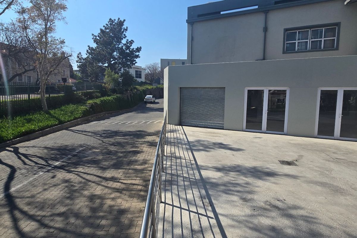 Exterior view of an industrial property featuring a paved driveway, roller shutter door, and double glass entrance doors.