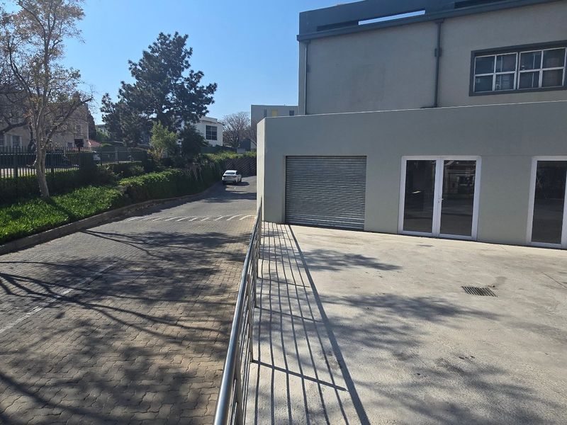 Exterior view of an industrial property featuring a paved driveway, roller shutter door, and double glass entrance doors.