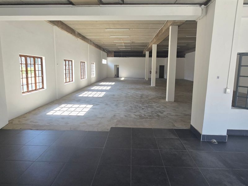 Spacious open-plan industrial unit featuring a mix of tiled and concrete flooring, exposed structural columns, and ample natural light through multi-pane windows.