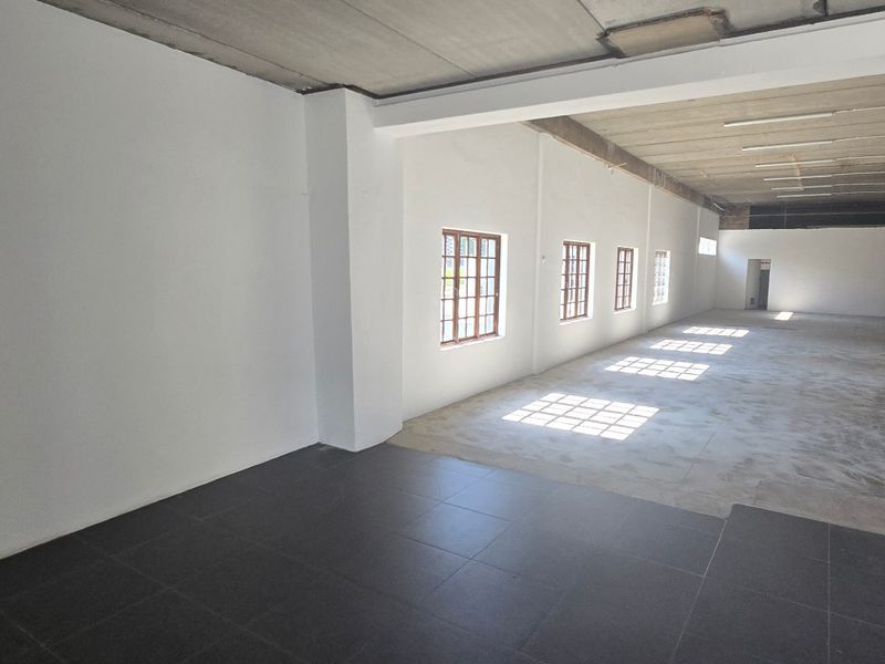 Spacious open-plan industrial unit featuring high exposed concrete ceilings, support columns, and a combination of tiled and concrete flooring with natural light.