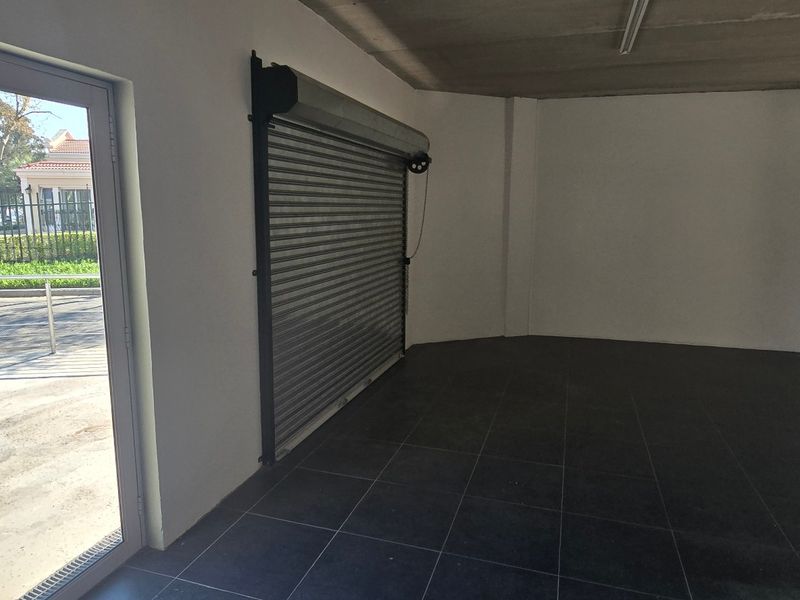 A clean, empty industrial garage space featuring dark tiled flooring, an exposed concrete ceiling, and a secure roller shutter door with exterior access.