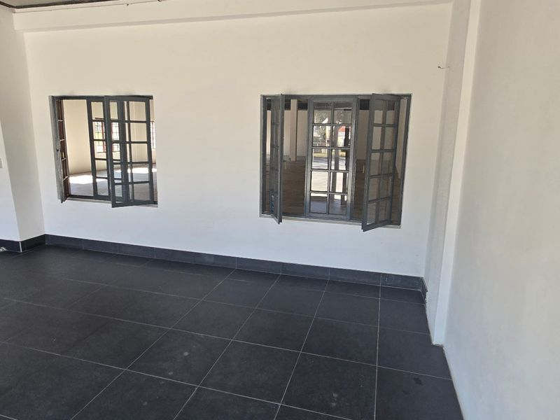 Spacious open-plan industrial area featuring dark tiled flooring, white walls, and multiple casement windows providing natural light.