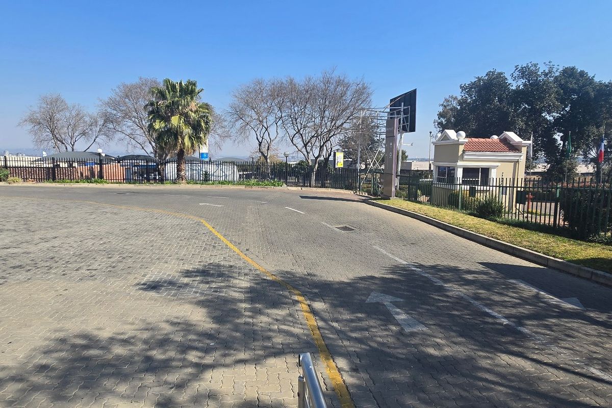 View of the industrial property entrance featuring a paved driveway, security guard house, and perimeter fencing.