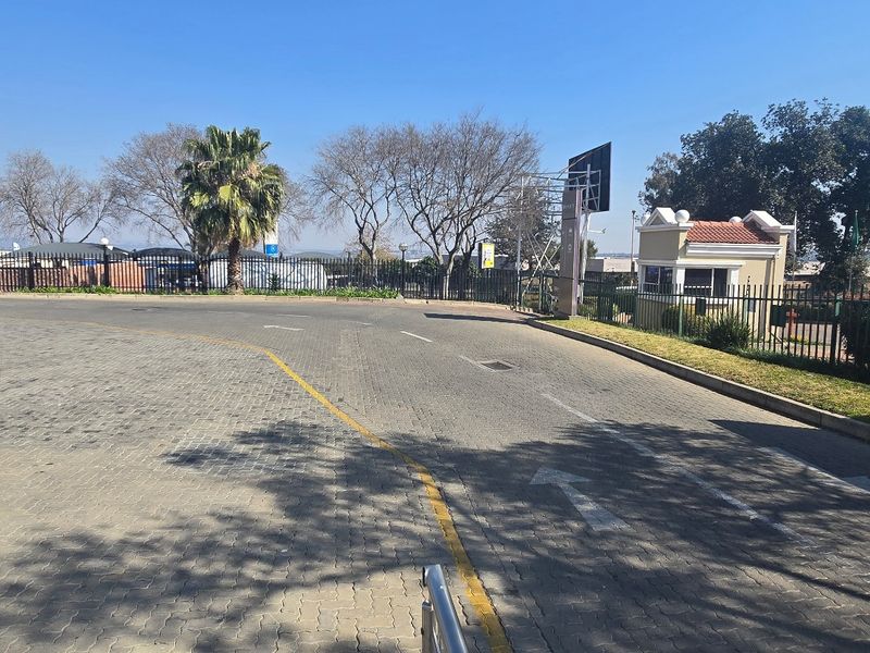 View of the industrial property entrance featuring a paved driveway, security guard house, and perimeter fencing.