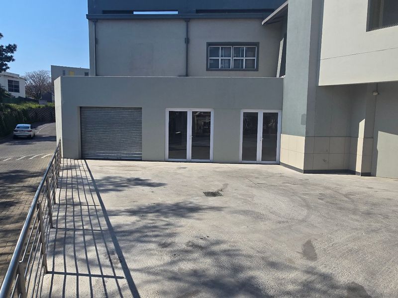 Exterior view of the industrial property featuring a concrete driveway, roller shutter door, and double glass entrance doors.