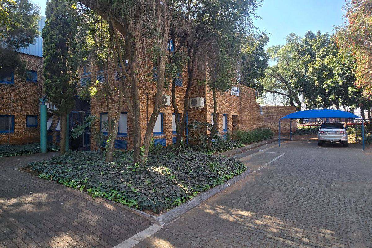 Front exterior view of an industrial property featuring a face brick facade, paved driveway, and covered parking area.