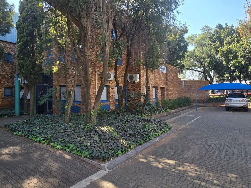 Front exterior view of an industrial property featuring a face brick facade, paved driveway, and covered parking area.