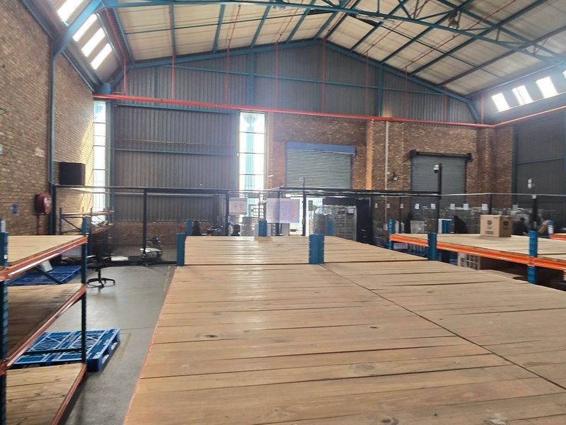 Spacious industrial warehouse featuring high ceilings with exposed steel trusses, brick walls, concrete flooring, and integrated heavy-duty racking systems.