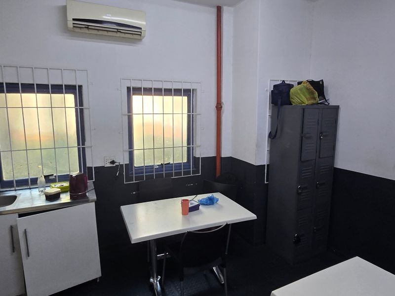 A functional utility or staff break room featuring a small kitchenette area, metal storage lockers, security window bars, and wall-mounted air conditioning.