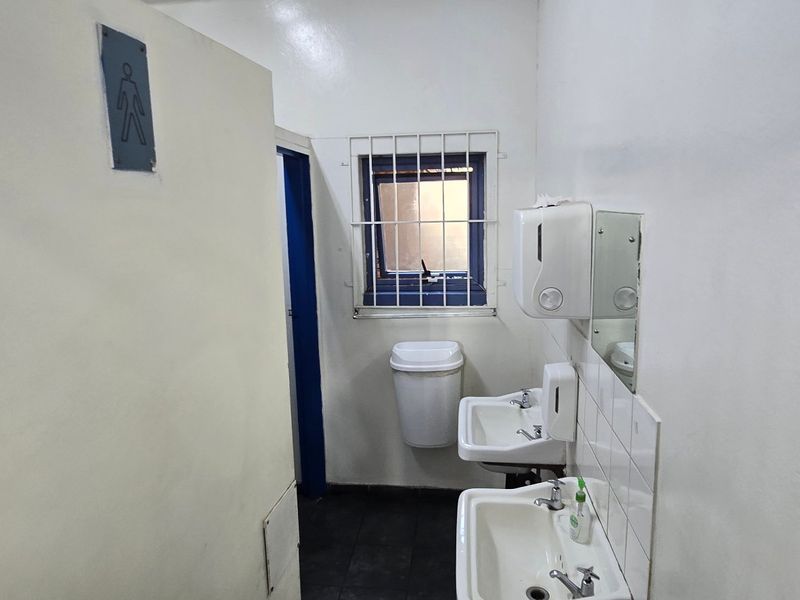 A functional industrial-style restroom featuring dual wall-mounted basins, security-barred window, and basic utility fixtures.