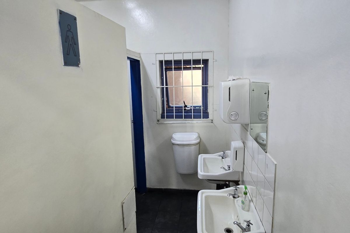 A functional industrial-style restroom featuring dual wall-mounted basins, security-barred window, and basic utility fixtures.