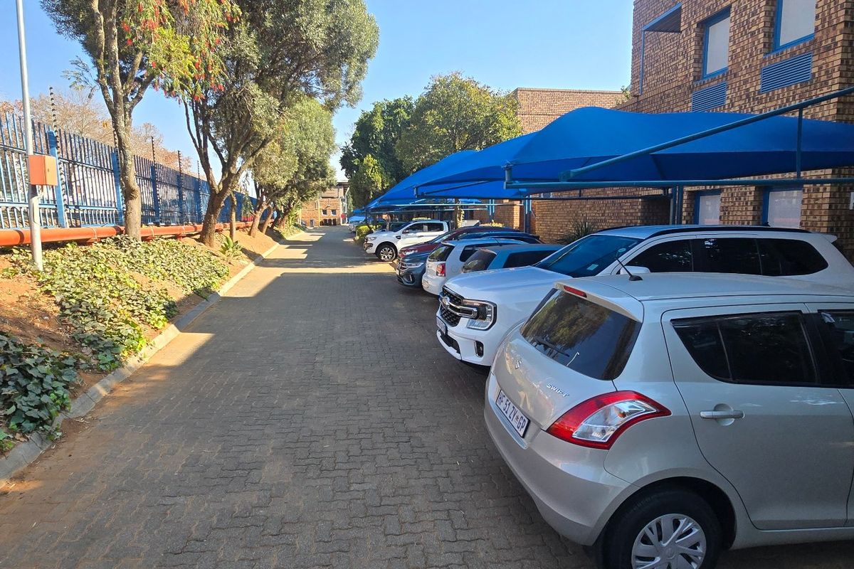 Exterior view of an industrial property featuring a paved driveway, secure electric fencing, and covered parking bays with blue shade cloth structures.