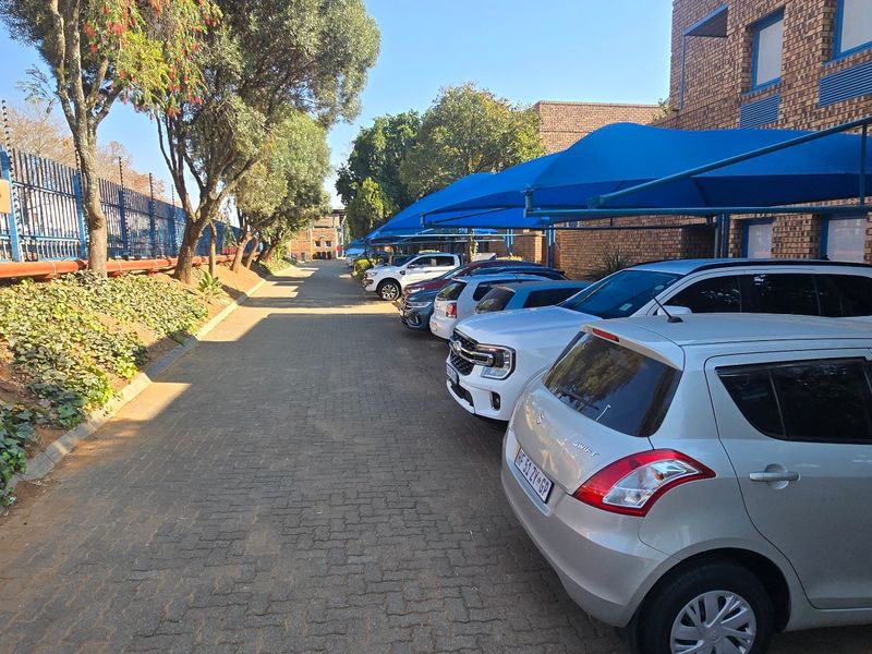 Exterior view of an industrial property featuring a paved driveway, secure electric fencing, and covered parking bays with blue shade cloth structures.