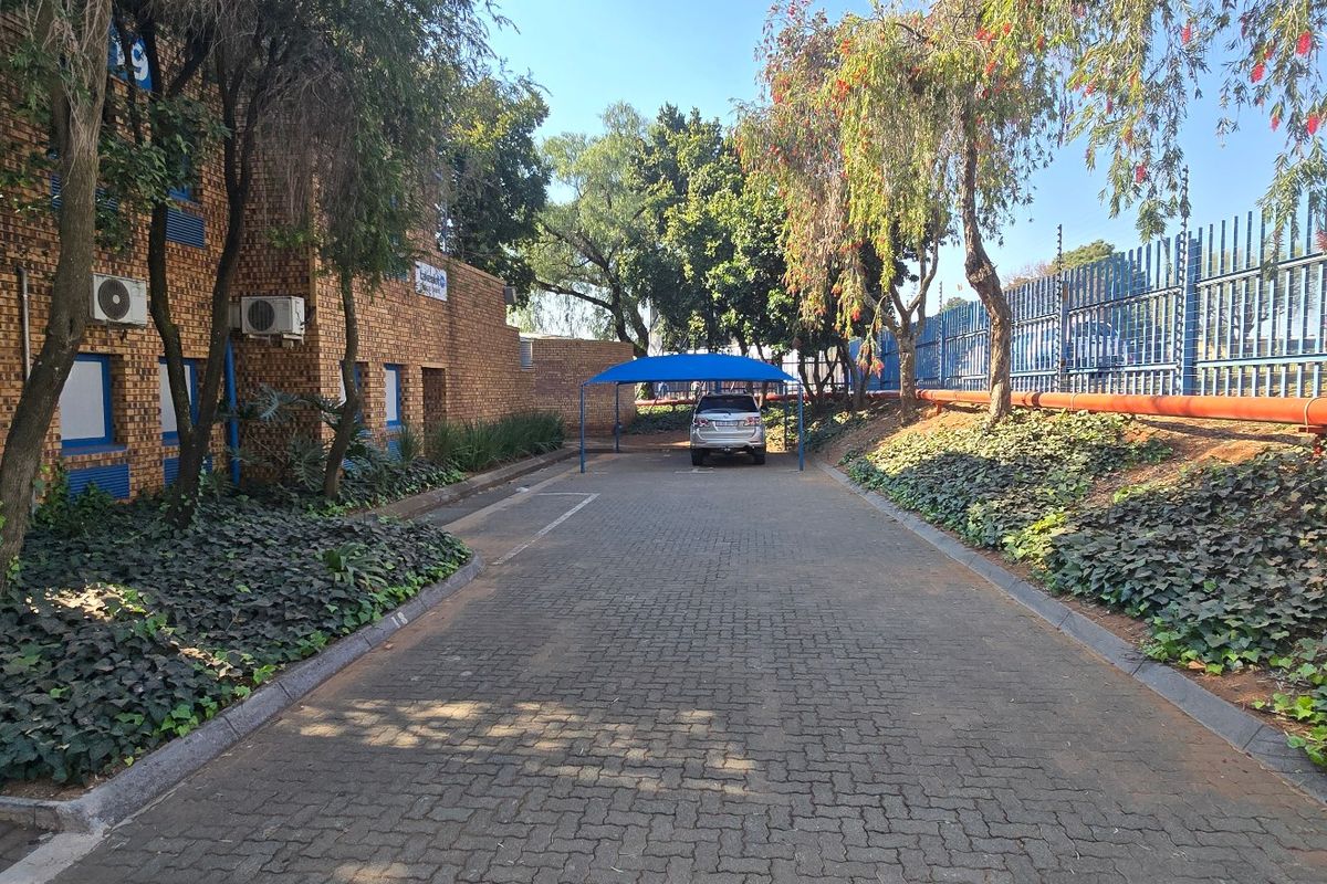 Industrial property exterior featuring a paved driveway, brick facade, secure perimeter fencing, and a covered carport area.