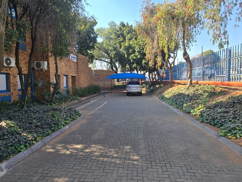 Industrial property exterior featuring a paved driveway, brick facade, secure perimeter fencing, and a covered carport area.