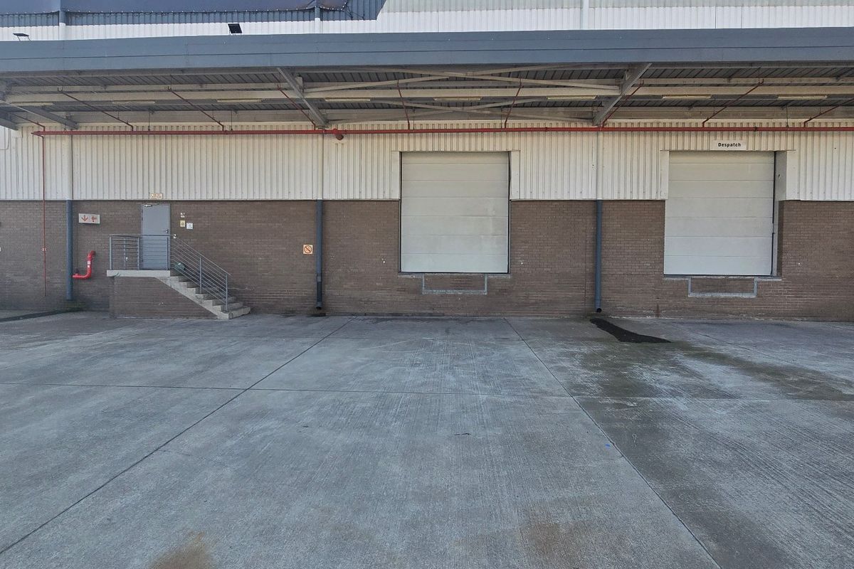 Industrial loading area featuring multiple roller shutter doors, a covered canopy, and a spacious concrete hardstand for logistics and dispatch operations.