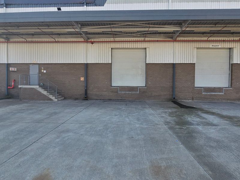Industrial loading area featuring multiple roller shutter doors, a covered canopy, and a spacious concrete hardstand for logistics and dispatch operations.