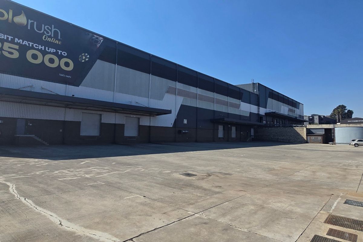 Large industrial warehouse exterior featuring a spacious concrete yard, multiple loading docks, and roller shutter doors, suitable for logistics or manufacturing operations.