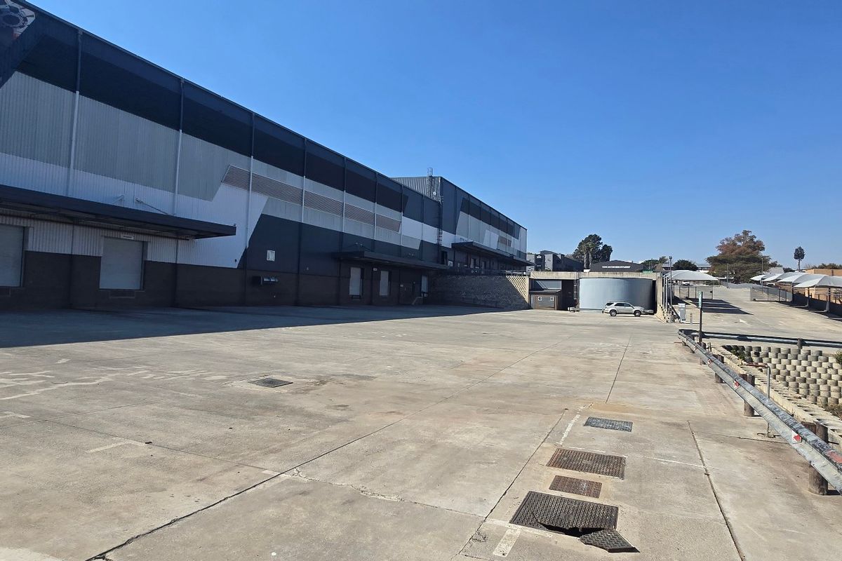 Spacious industrial concrete loading yard featuring a large warehouse facade with multiple loading bays and a retaining wall.