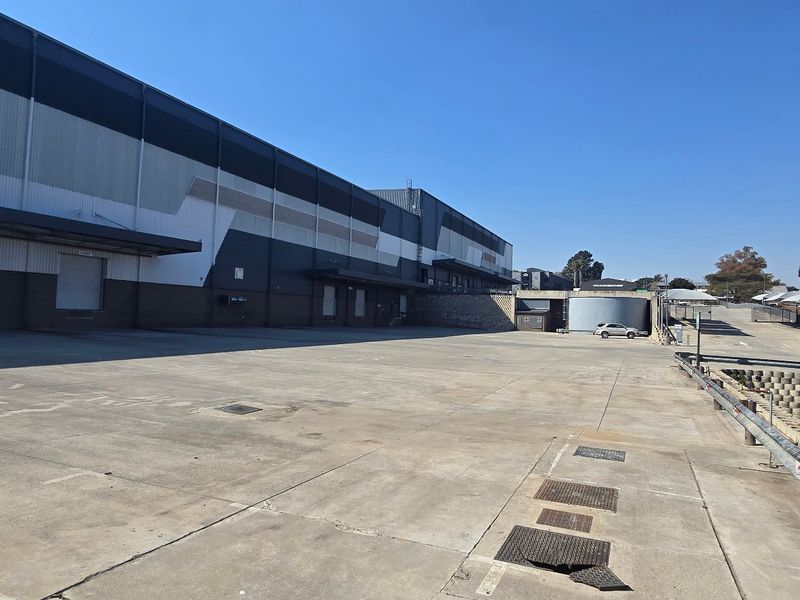 Spacious industrial concrete loading yard featuring a large warehouse facade with multiple loading bays and a retaining wall.