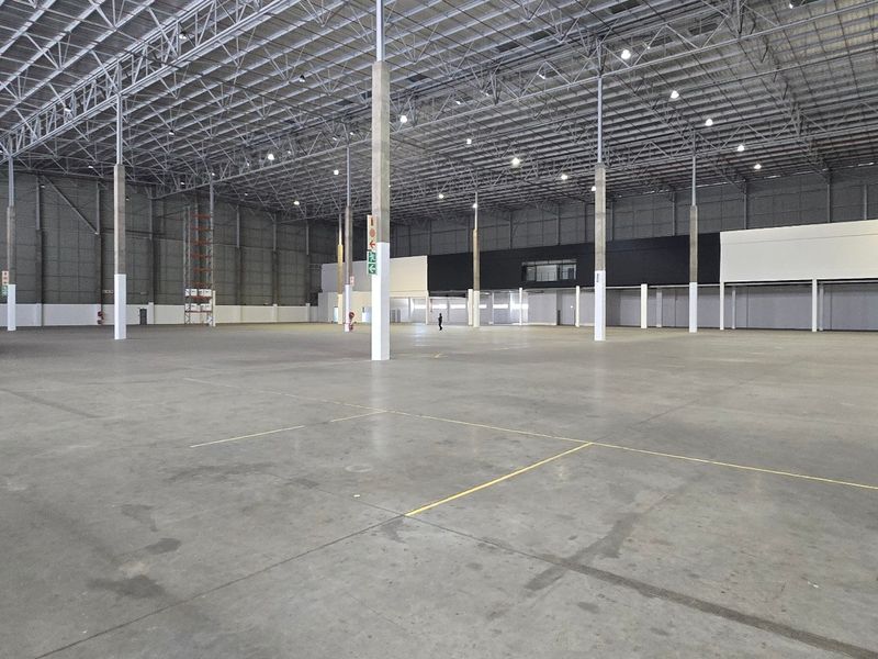 A spacious, open-plan industrial warehouse featuring high ceilings, exposed steel trusses, polished concrete flooring, and high-bay lighting, suitable for logistics or manufacturing operations.