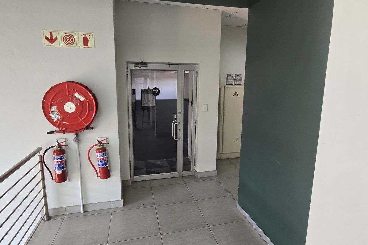 A clean commercial entry area featuring tiled flooring, a glass door, and essential fire safety equipment including a hose reel and extinguishers.