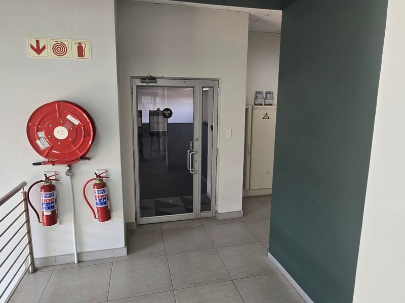 A clean commercial entry area featuring tiled flooring, a glass door, and essential fire safety equipment including a hose reel and extinguishers.