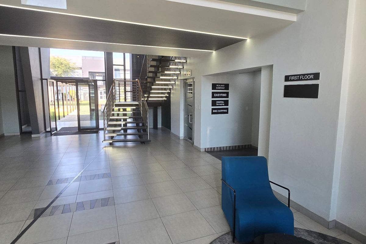 Modern commercial building entrance lobby featuring tiled flooring, a prominent staircase, and clear directional signage for office tenants.