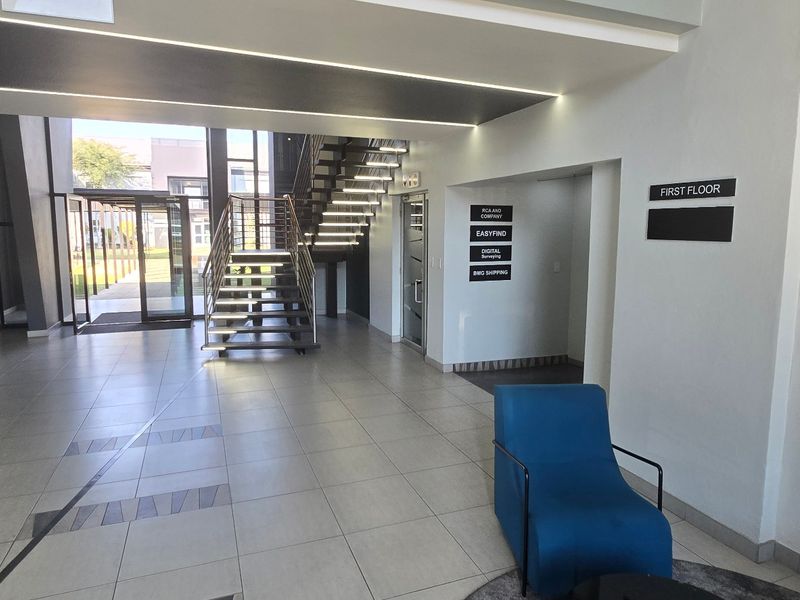 Modern commercial building entrance lobby featuring tiled flooring, a prominent staircase, and clear directional signage for office tenants.