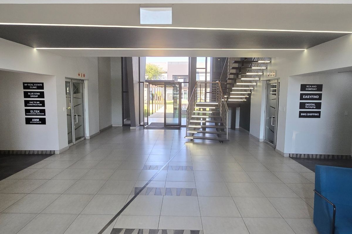 Modern commercial building entrance lobby featuring tiled flooring, recessed linear lighting, a central staircase, and clear tenant directory signage.