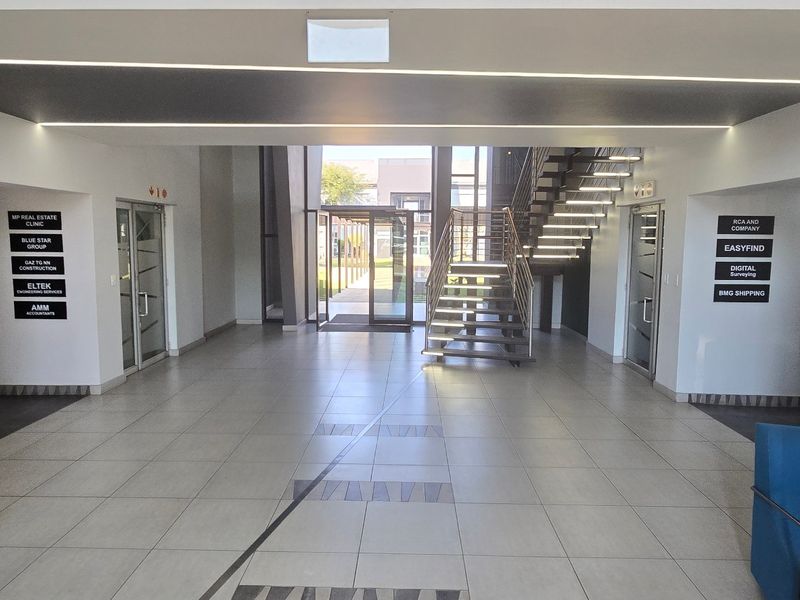 Modern commercial building entrance lobby featuring tiled flooring, recessed linear lighting, a central staircase, and clear tenant directory signage.