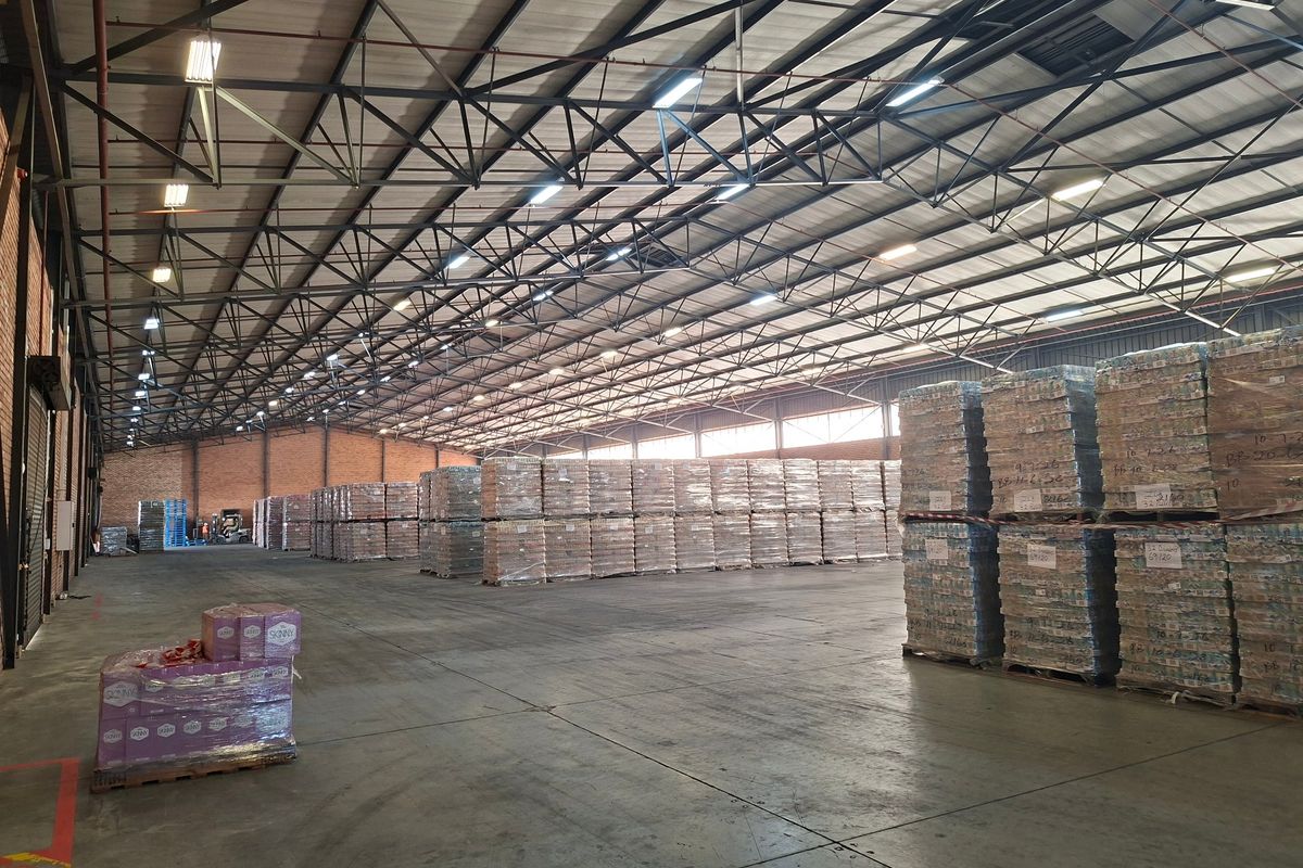 Spacious industrial warehouse featuring high-clearance steel roof trusses, durable concrete flooring, and functional brick walling, suitable for large-scale storage or distribution operations.