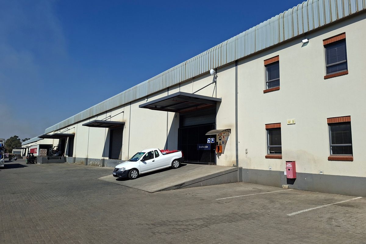 Industrial warehouse exterior featuring multiple loading bays with roller shutter doors, concrete ramps, and a paved yard area for logistics operations.