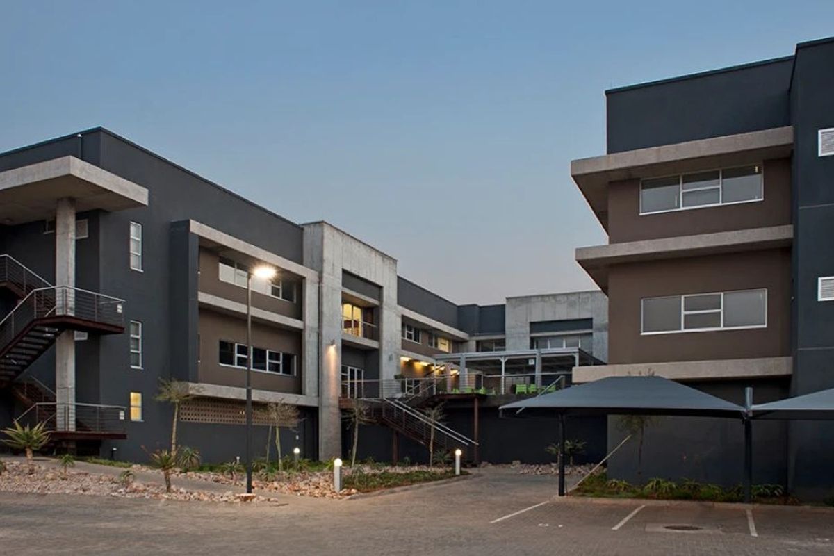 Modern commercial office complex featuring contemporary concrete and dark-toned facade, external staircases, paved parking area, and integrated carports.