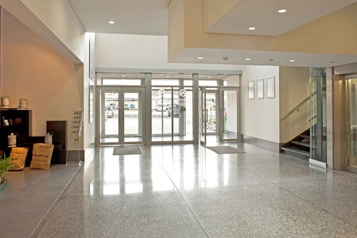 Spacious commercial building lobby featuring polished terrazzo flooring, glass entrance doors, and integrated elevator access with a modern suspended ceiling design.
