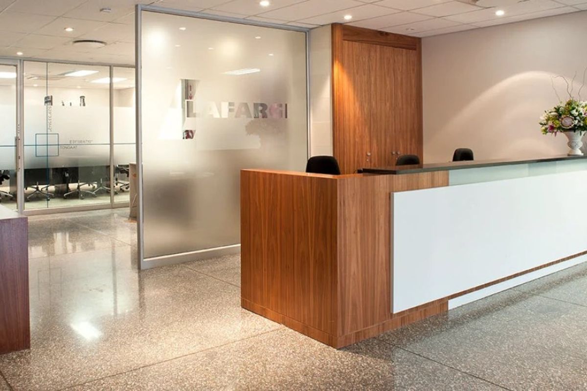 Modern commercial reception area featuring a sleek wood and white reception desk, polished terrazzo flooring, and a frosted glass partition wall.
