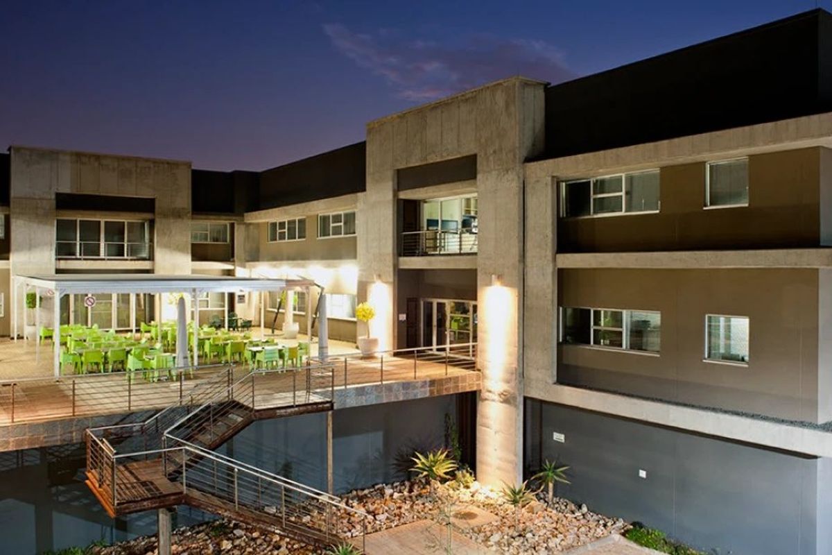 Modern commercial building exterior featuring a multi-level design with a spacious covered patio, metal staircase, and contemporary concrete and panel finishes.
