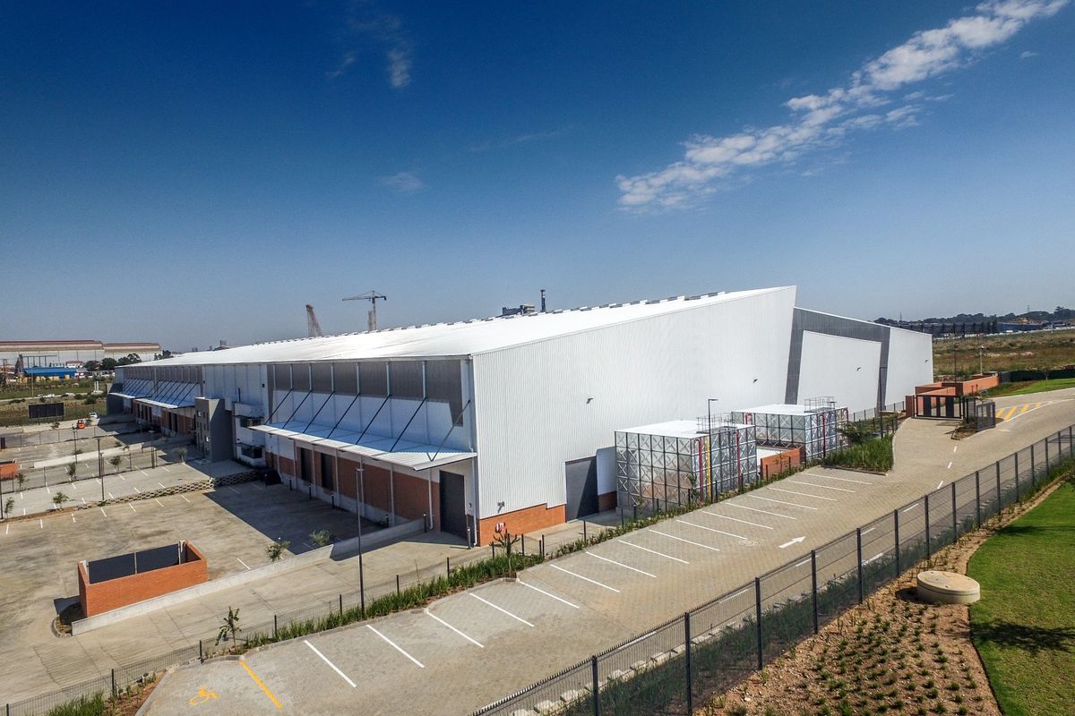 Aerial view of a modern industrial warehouse facility featuring extensive parking, secure perimeter fencing, and dedicated loading bay access.
