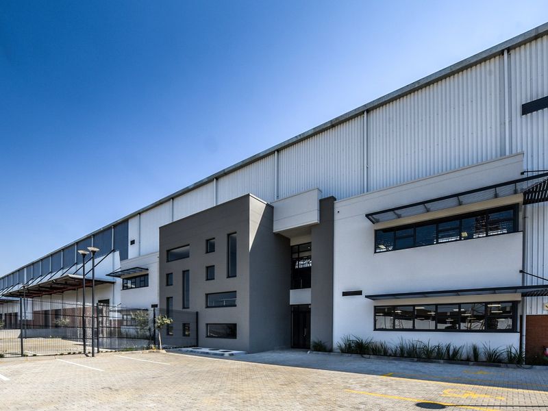 Modern industrial warehouse facility featuring a clean facade with corrugated metal cladding, paved parking area, and professional architectural design.