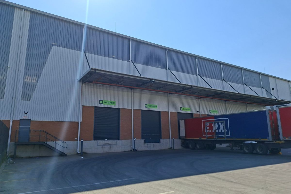 Industrial warehouse exterior featuring multiple roller shutter loading bays, a protective canopy, and a spacious concrete yard for logistics and transport operations.