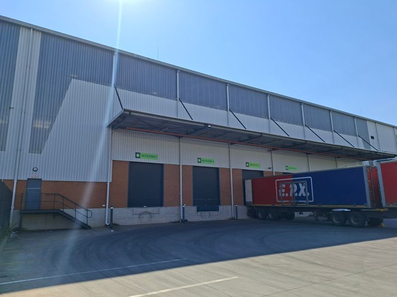 Industrial warehouse exterior featuring multiple roller shutter loading bays, a protective canopy, and a spacious concrete yard for logistics and transport operations.