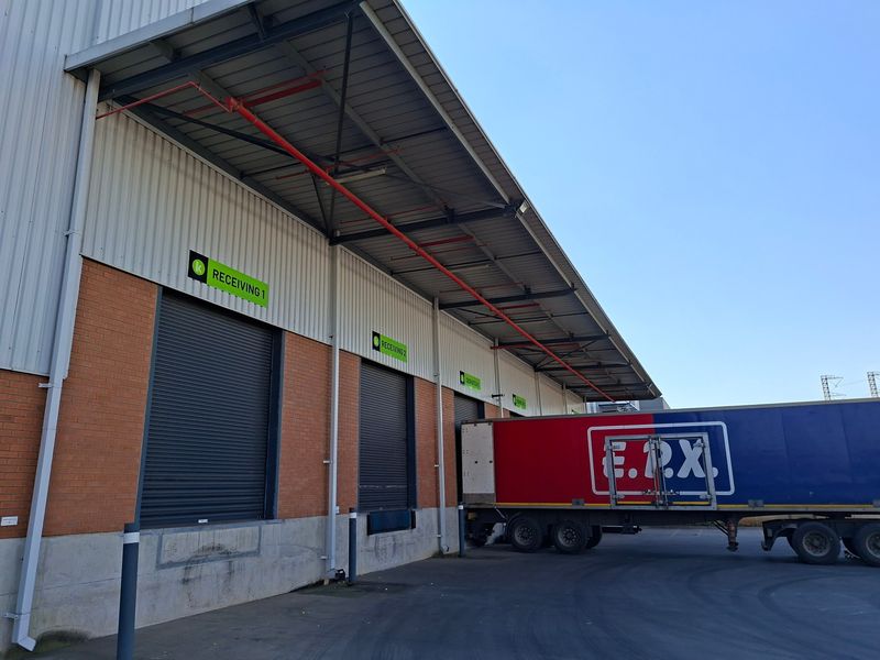 Industrial warehouse exterior featuring multiple loading docks with roller shutter doors, metal cladding, and exposed fire suppression systems.