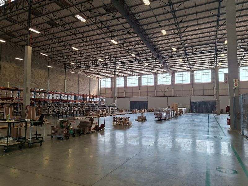 Spacious industrial warehouse featuring high ceilings with exposed steel trusses, polished concrete floors, and large windows providing ample natural light.
