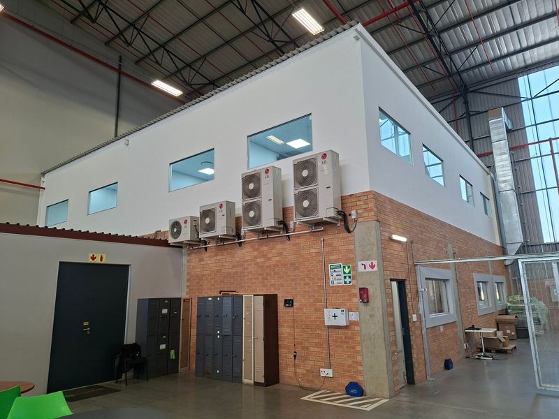 Industrial warehouse interior featuring exposed brickwork, high-clearance steel roof trusses, integrated air conditioning units, and functional locker storage area.
